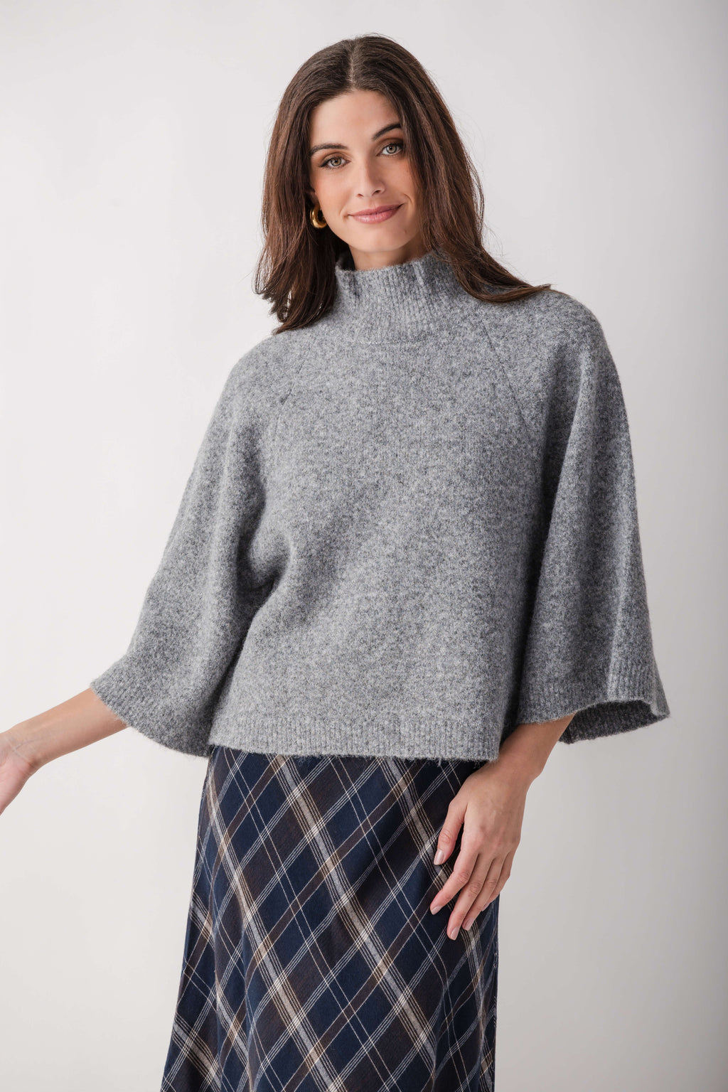 Gray turtleneck sweater with three-quarter bell sleeves worn with a navy plaid skirt.