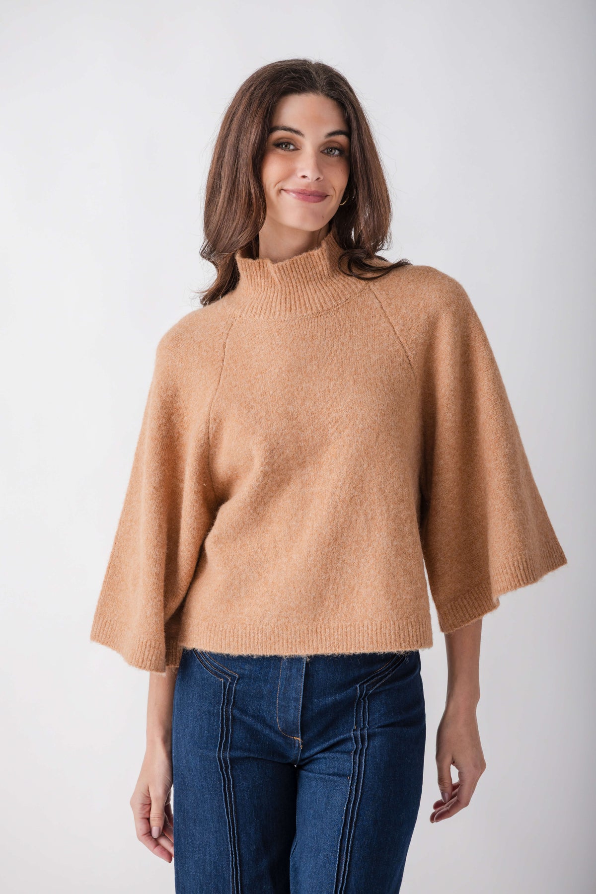 Camel turtleneck sweater with three-quarter sleeves worn over dark denim jeans.