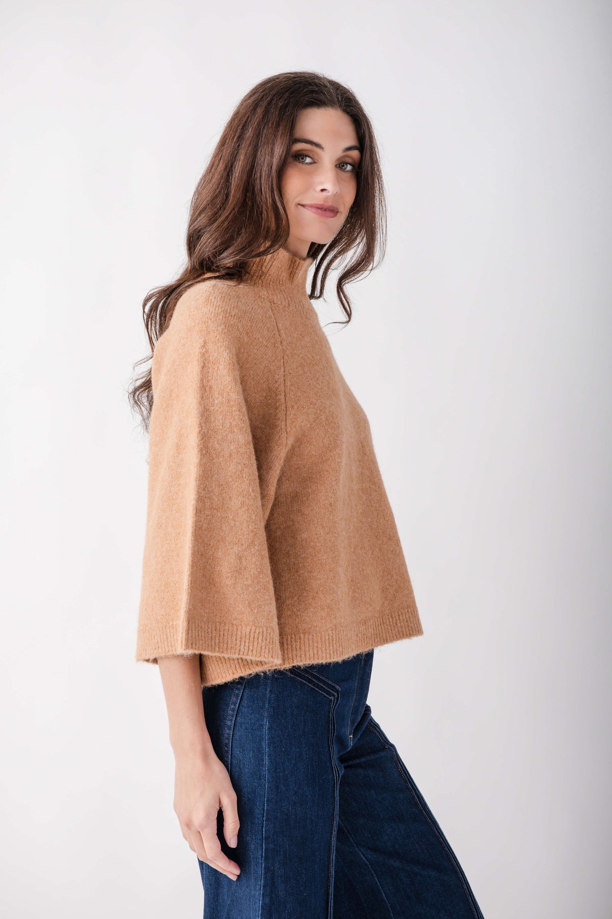 Beige turtleneck sweater with striped trim worn with dark jeans, shown from the back.