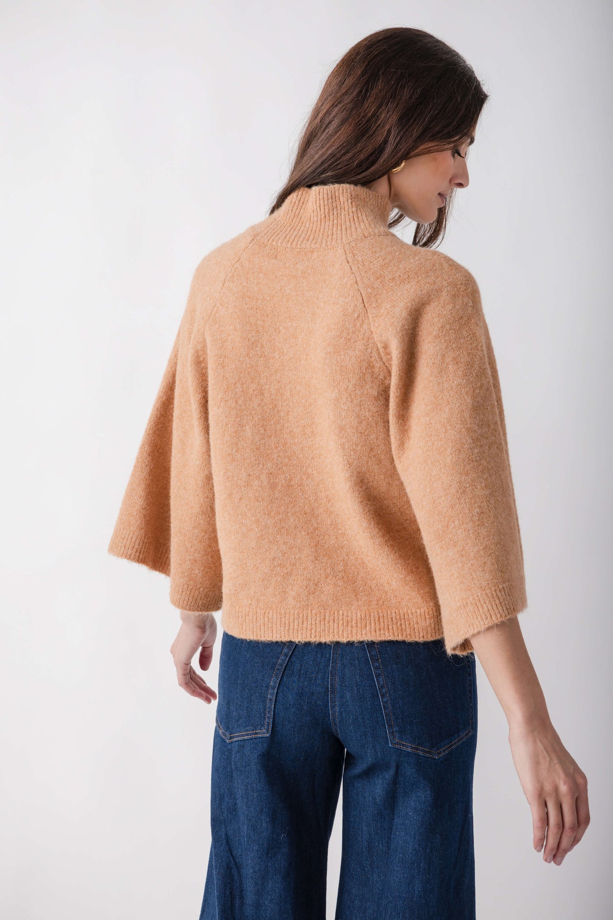 Beige turtleneck sweater with three-quarter sleeves worn with dark blue jeans, shown from the back.