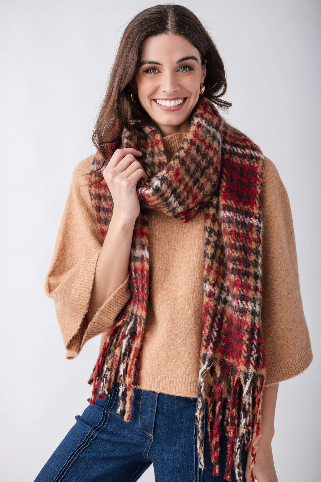 Red, black, and tan houndstooth patterned scarf with fringe trim worn draped around shoulders.