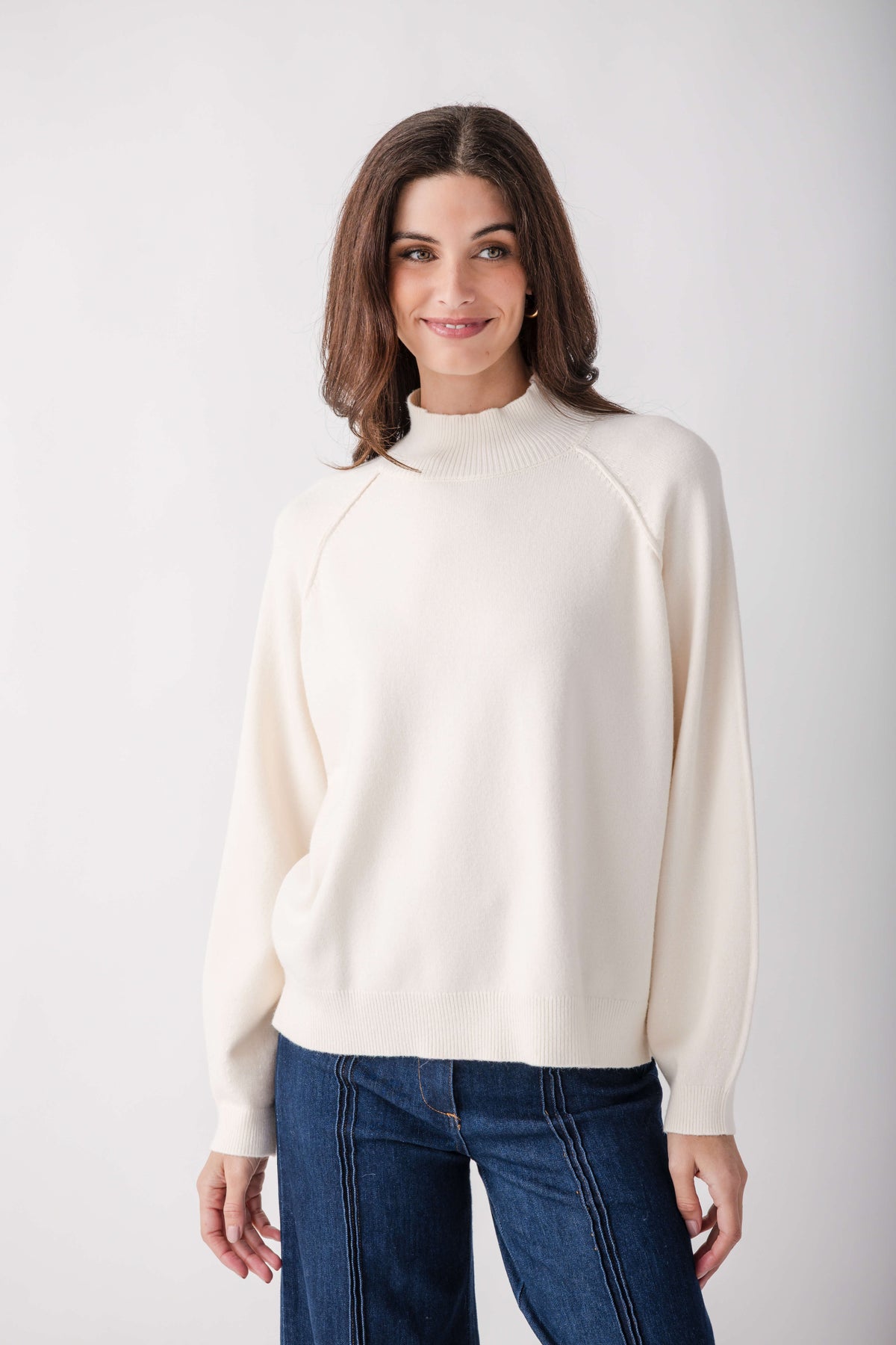 Cream knit sweater with mock turtleneck and long sleeves worn with dark blue jeans.