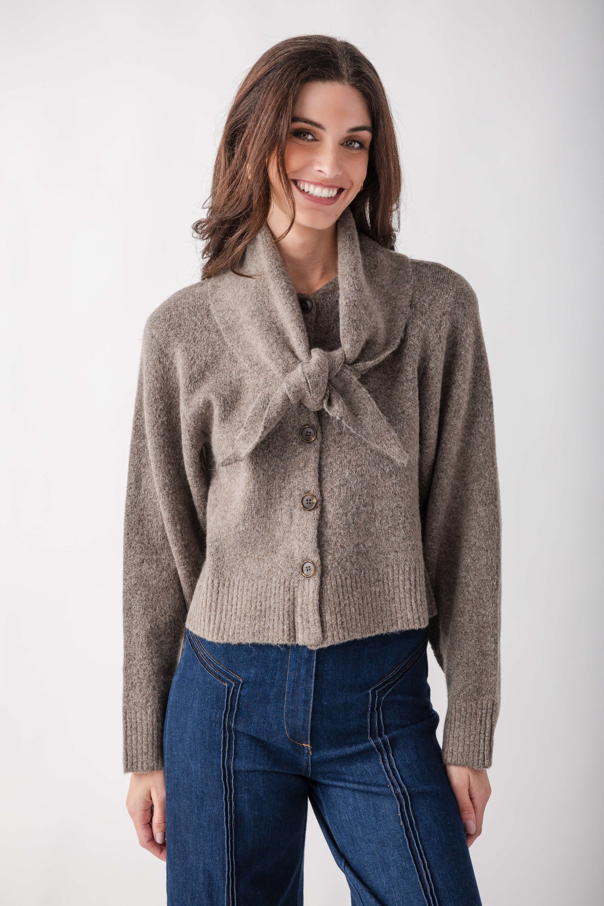 Beige knit cardigan with detachable scarf collar and button front, styled with dark jeans.