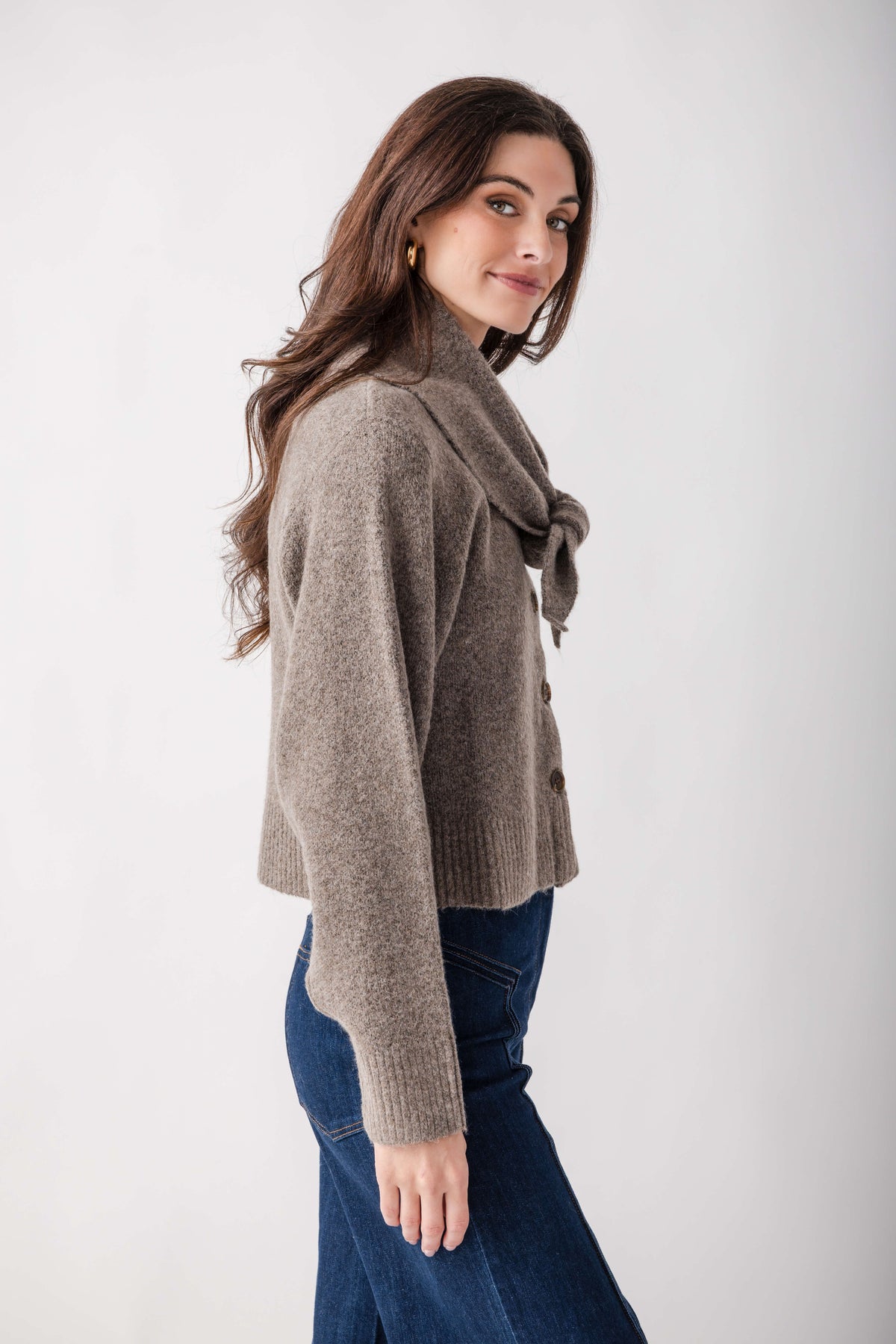 Taupe knit cardigan with detachable scarf wrap, worn with dark blue jeans.