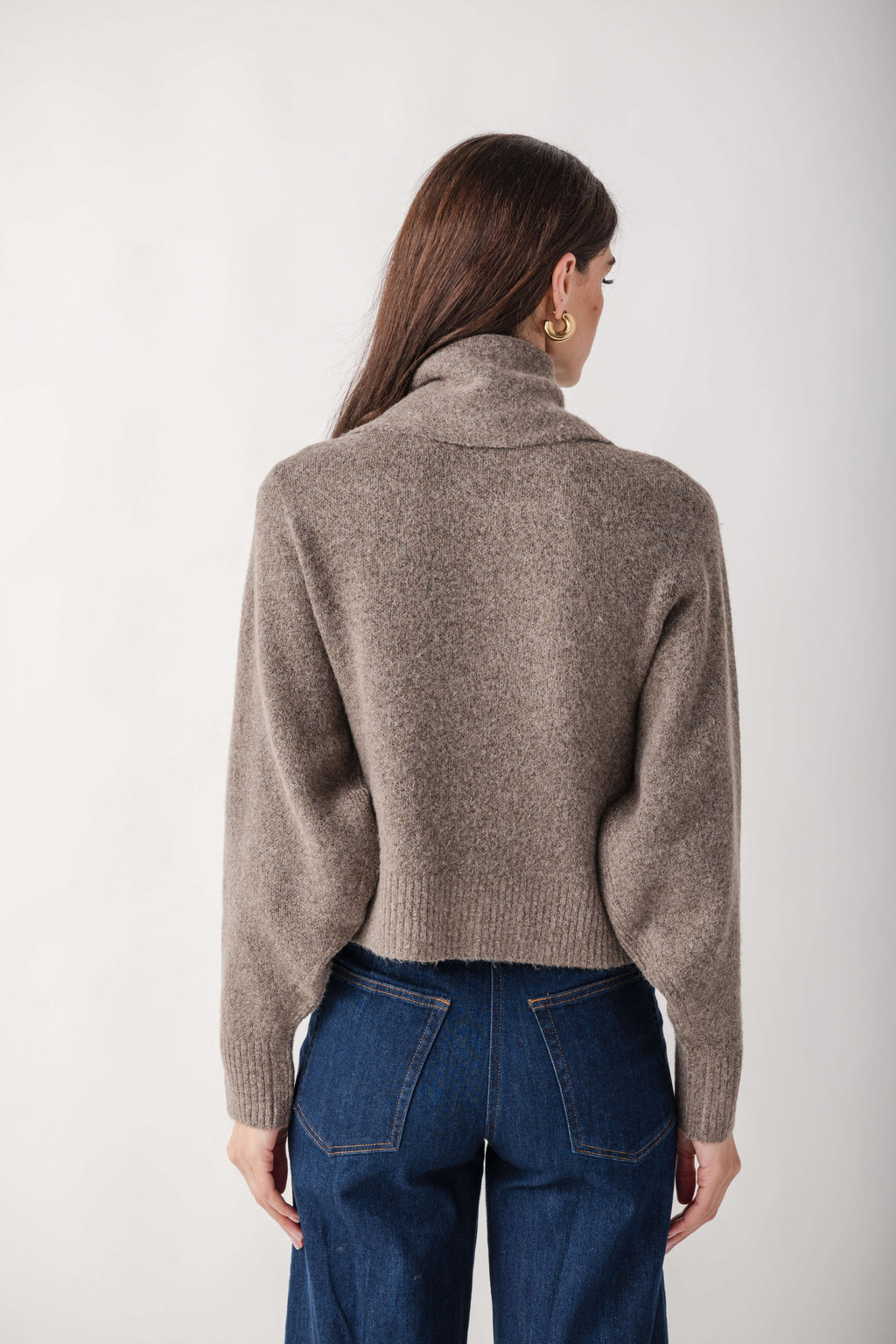 Beige knit cardigan with turtleneck collar worn over dark blue jeans, shown from back view.