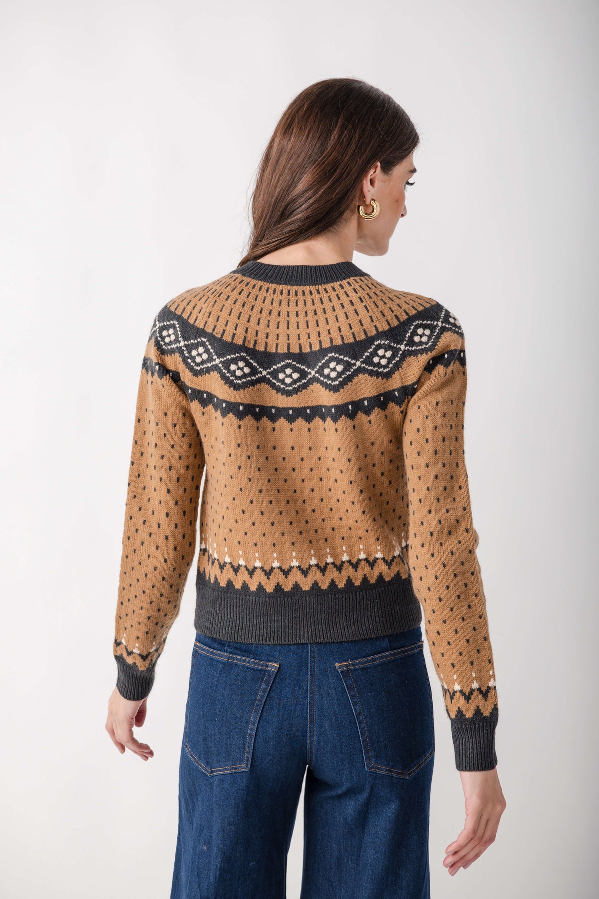 Tan and charcoal knit cardigan with geometric patterned yoke and wavy stripe detail at hem, worn with blue jeans.