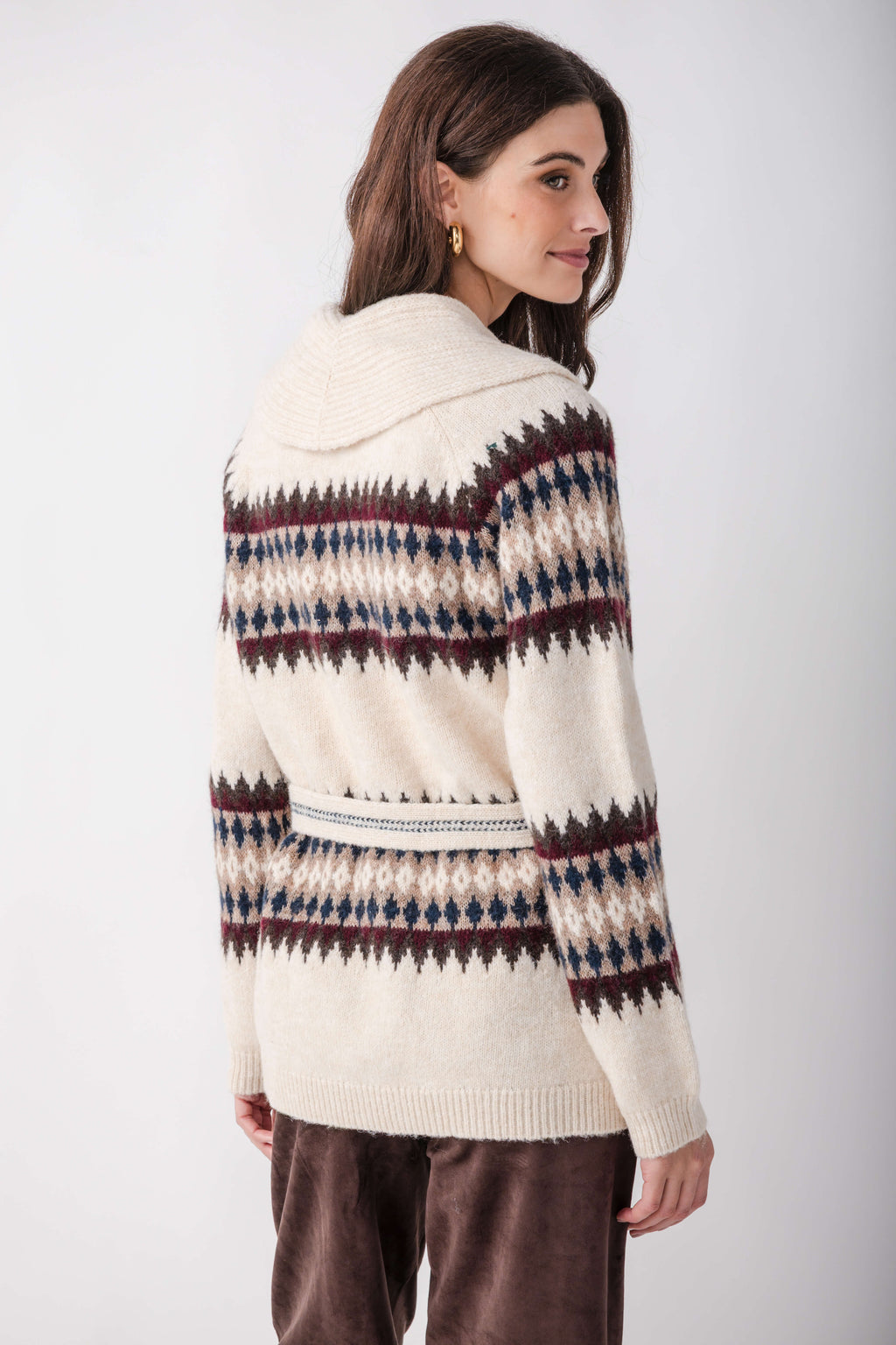 Cream cardigan with navy, burgundy, and tan geometric patterning across shoulders and waist, worn with brown pants.