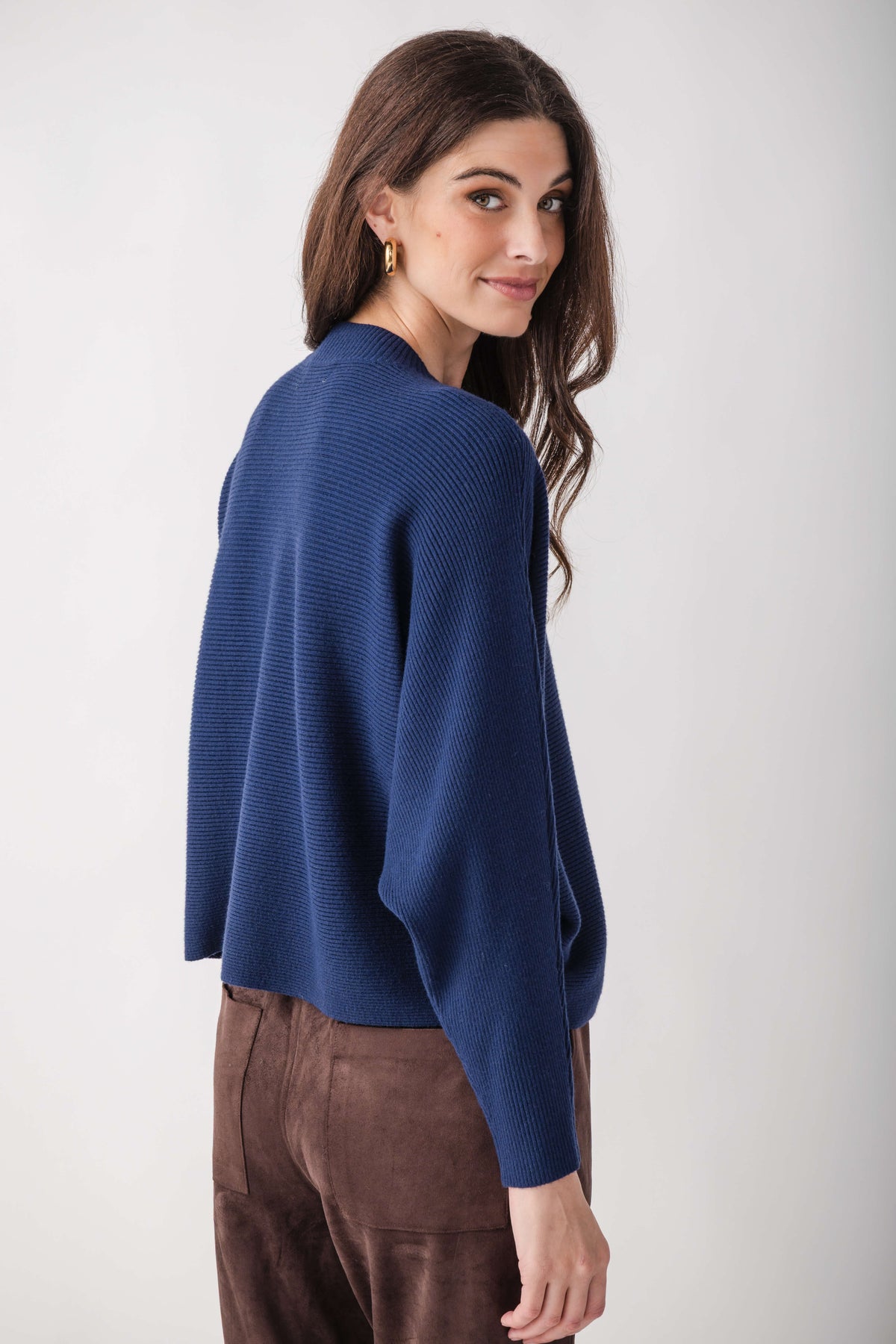Woman wearing blue ribbed crewneck sweater with dolman sleeves and brown trousers, shown from back angle.