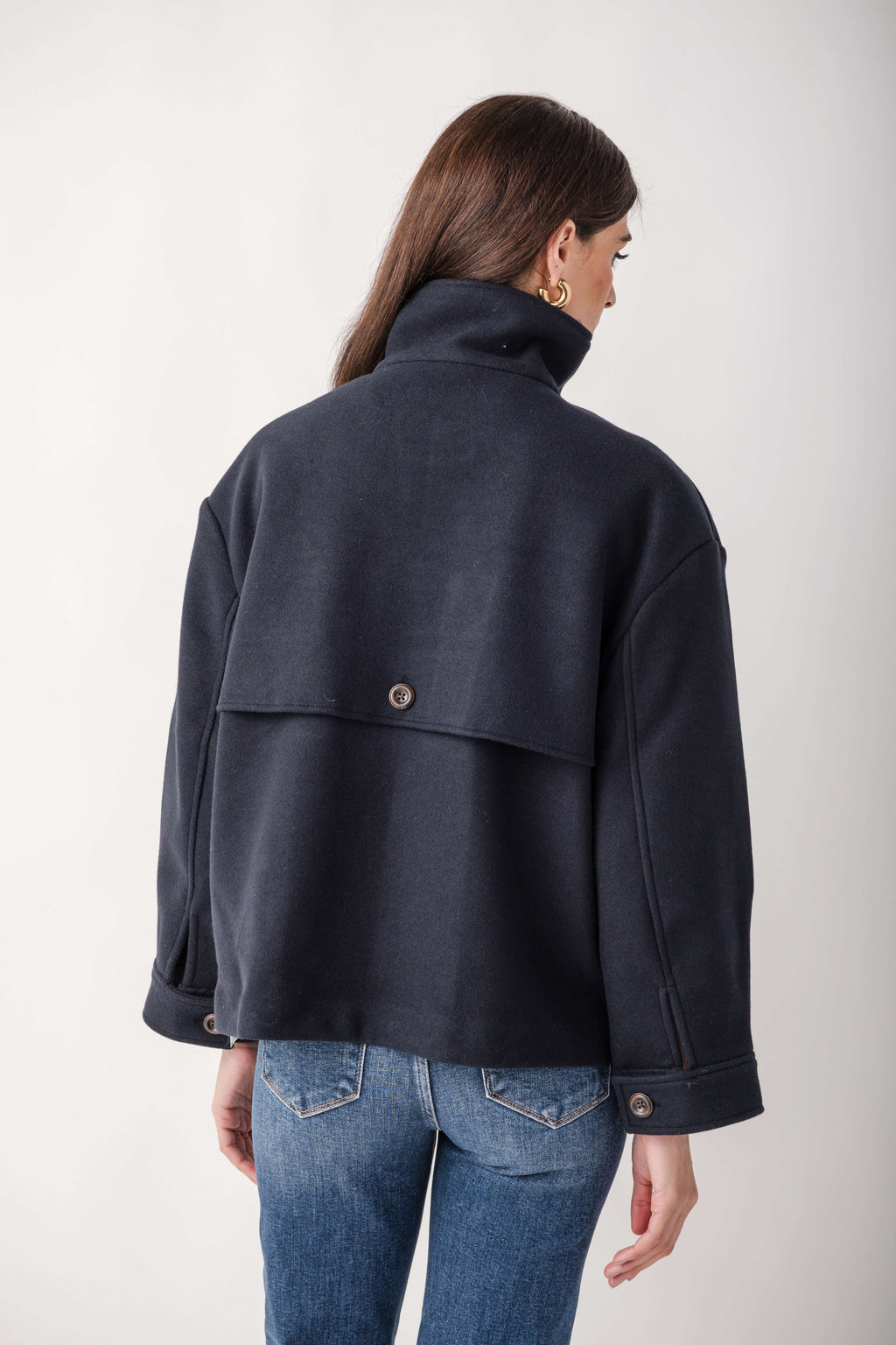 Woman wearing a dark navy double-breasted melton jacket with a high collar, shown from back, paired with blue jeans.