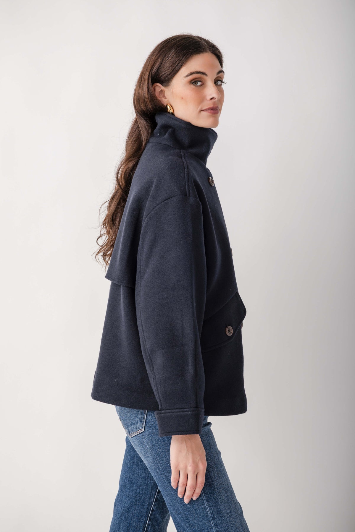 Navy wool melton double-breasted jacket with high collar and button closure, worn over blue jeans.