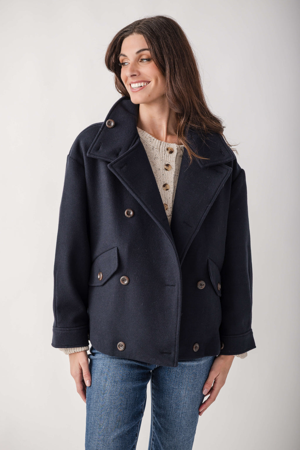 Navy double-breasted wool jacket with notch lapels, patch pockets, and horn buttons worn over a cream cable-knit top.