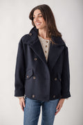 Navy double-breasted wool jacket with notch lapels, patch pockets, and horn buttons worn over a cream cable-knit top.