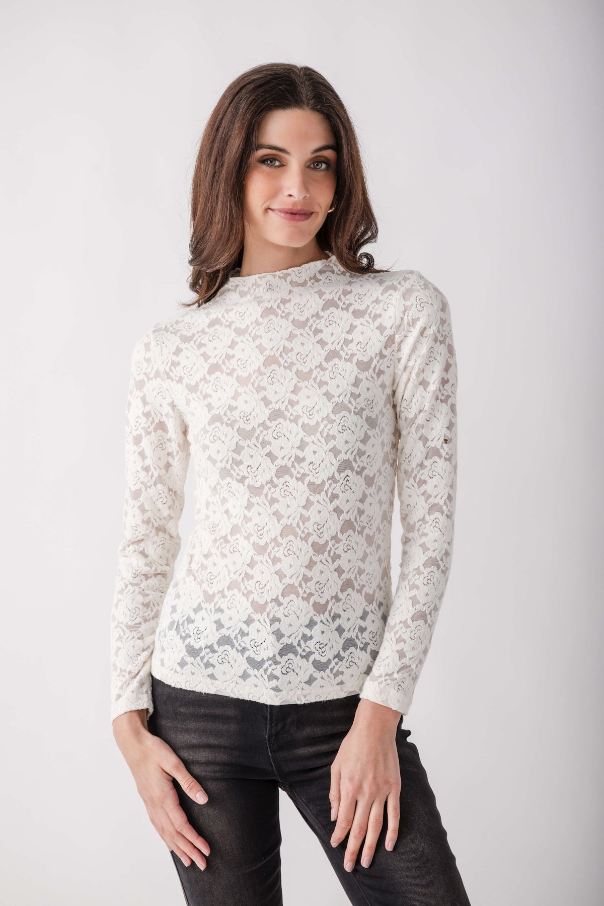 Cream lace long-sleeve mockneck top with scrollwork pattern worn with black jeans.