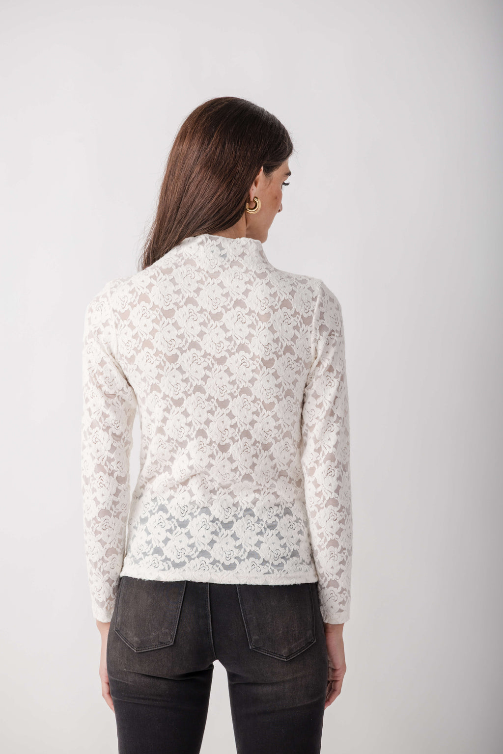 White lace long-sleeve mockneck top with allover floral pattern worn with dark jeans.
