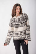 A woman wears a cream knit sweater with black Nordic geometric patterns, wide sleeves, and a crew neckline, paired with black pants.