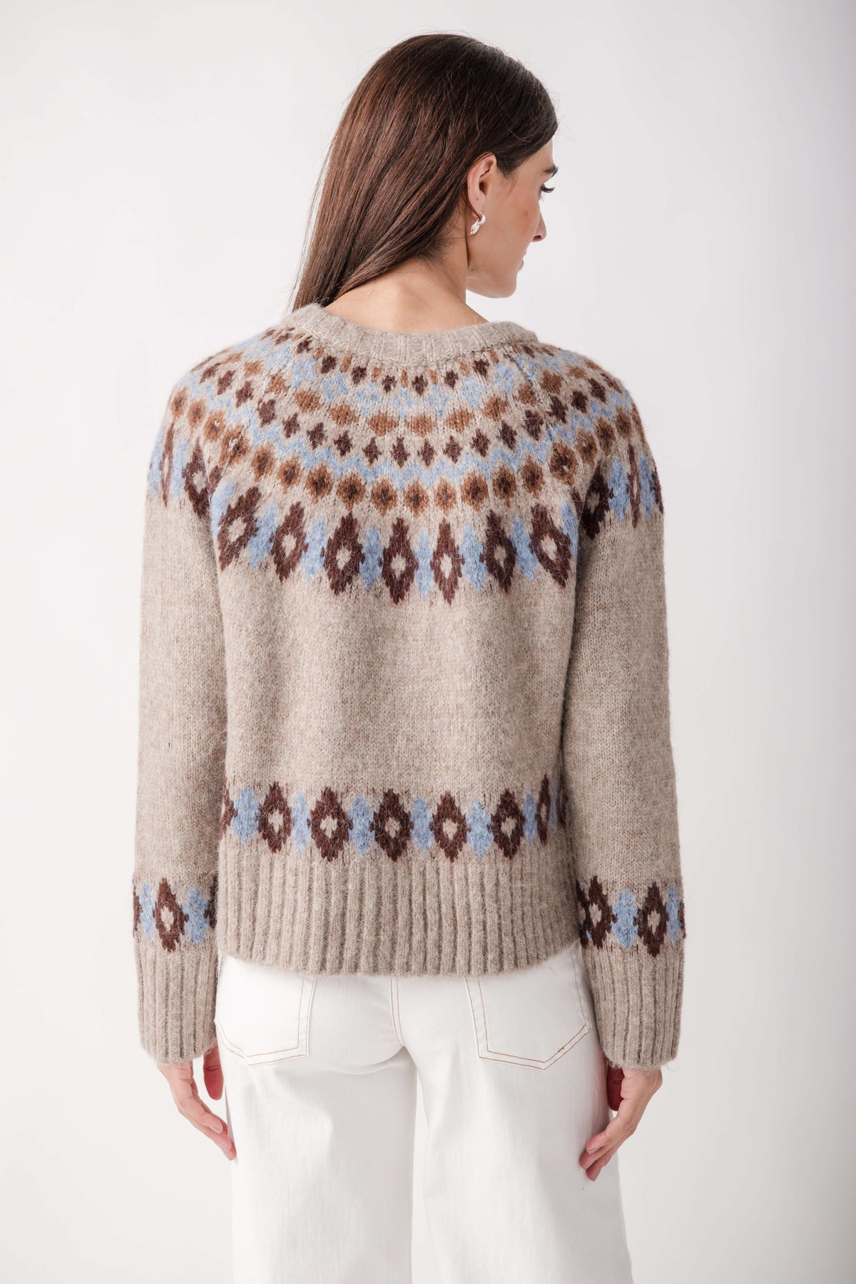 Back view of a woman wearing a beige knit cardigan with brown and blue Fair Isle patterns, paired with white pants.