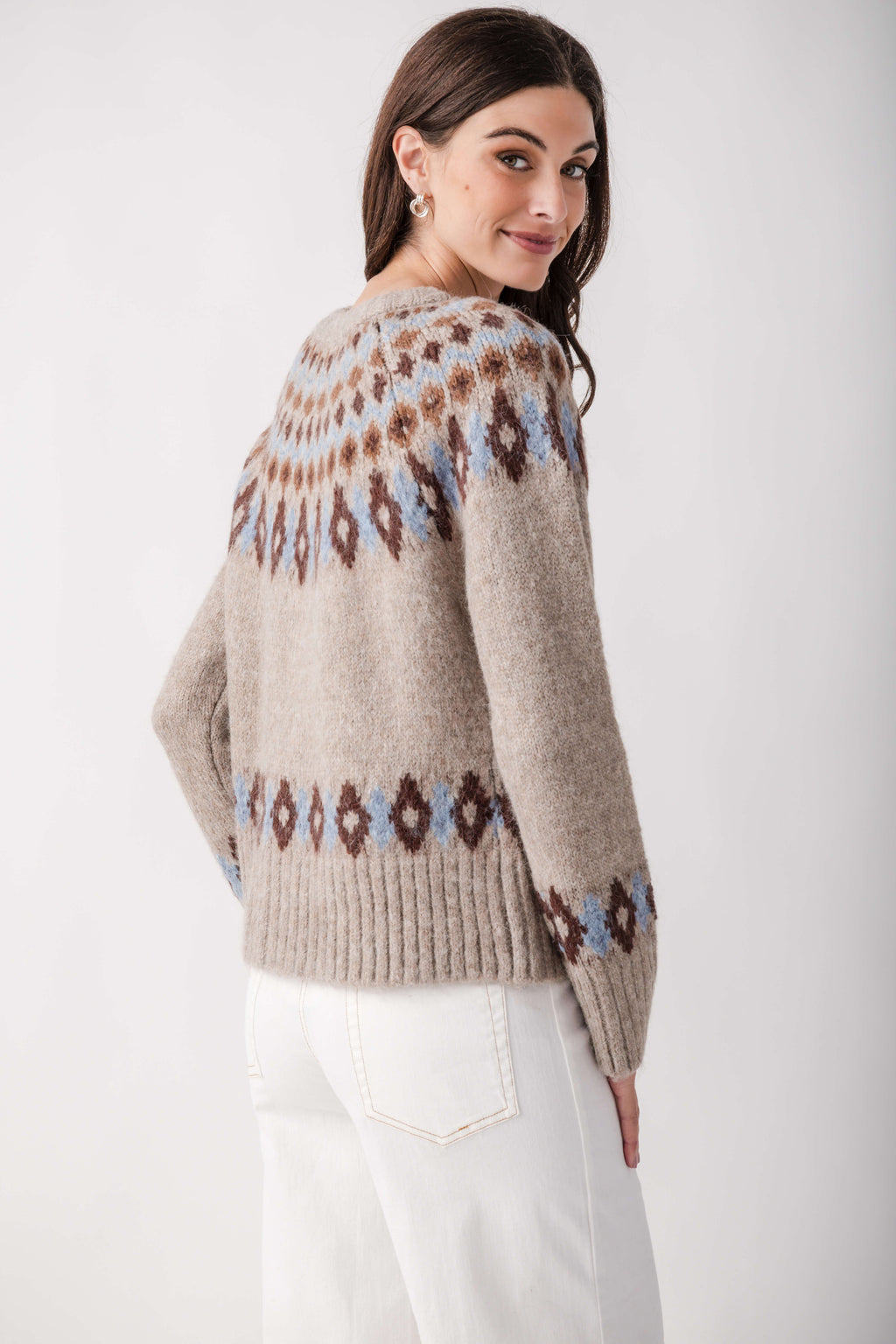 A woman seen from behind wears a beige Fair Isle cardigan with blue and brown patterns and white pants.