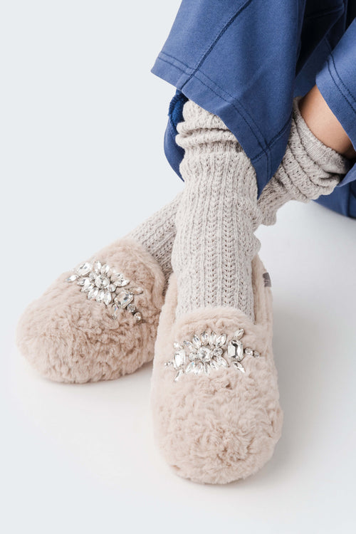 Light beige fuzzy slipper with ribbed knit cuff and silver floral jewel applique on the side.