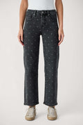 A model from the waist down wearing dark gray washed jeans with a small light gray polka dot pattern, paired with beige sneakers, against a light gray studio background.