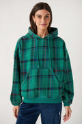 A woman wears a green plaid hooded sweatshirt with red and black stripes, a front pouch pocket, and navy velour pants.