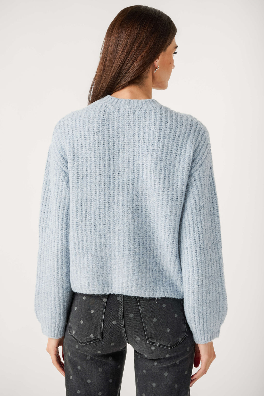 Back view of a woman wearing a light blue ribbed knit cardigan with full sleeves and dark gray polka dot jeans.