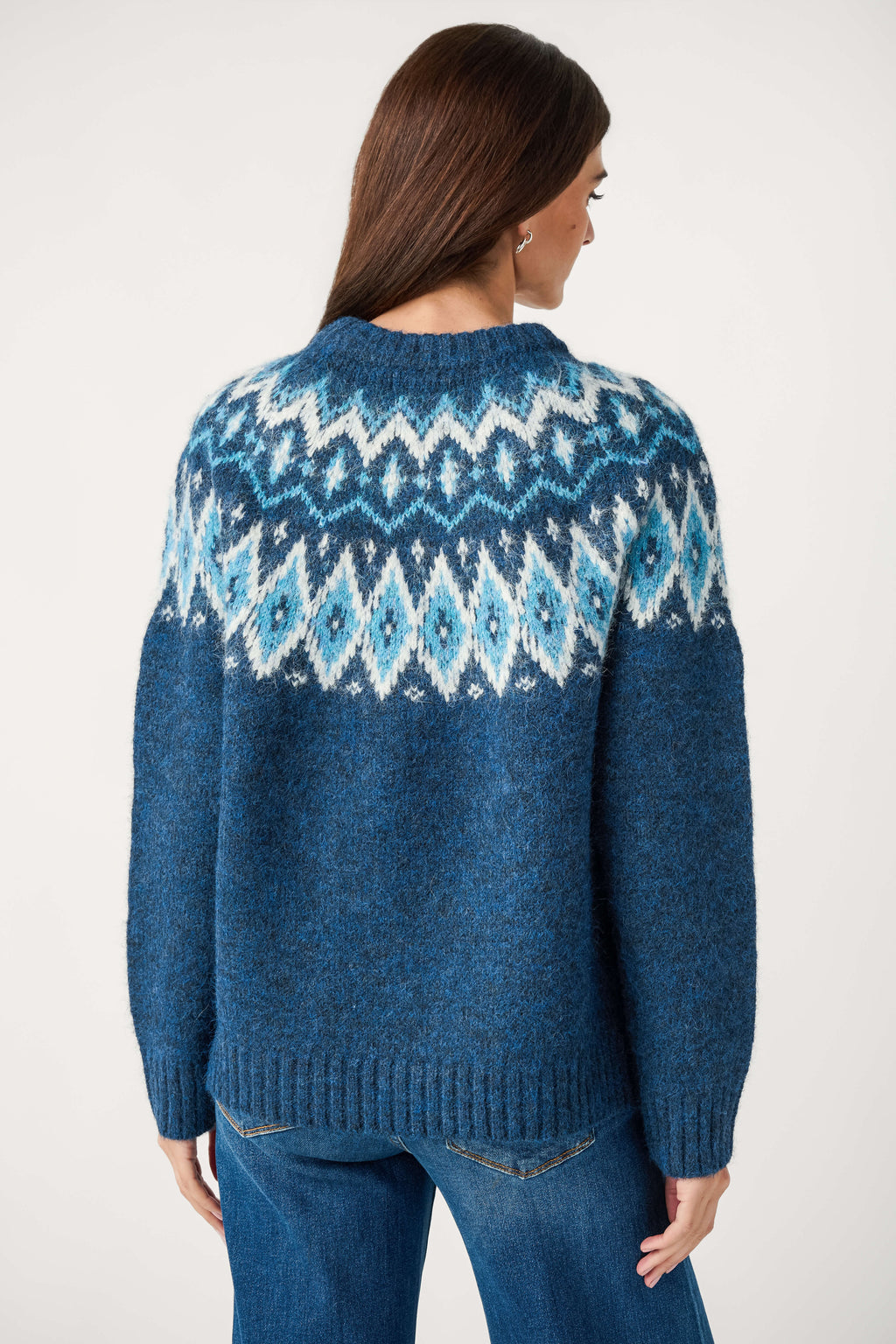 Back view of a woman wearing a blue knit crewneck sweater with a white and light blue Fair Isle yoke, paired with jeans.