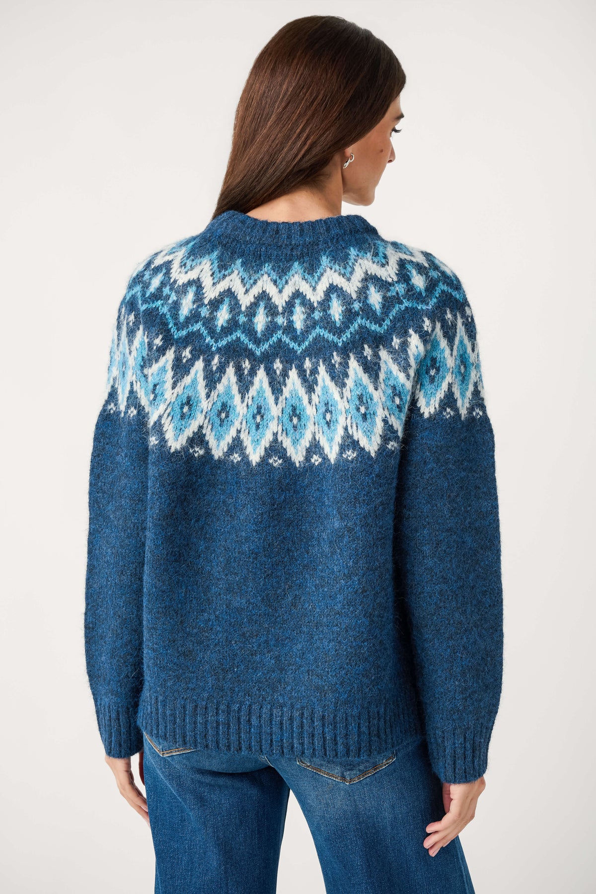 Back view of a woman wearing a blue knit crewneck sweater with a white and light blue Fair Isle yoke, paired with jeans.