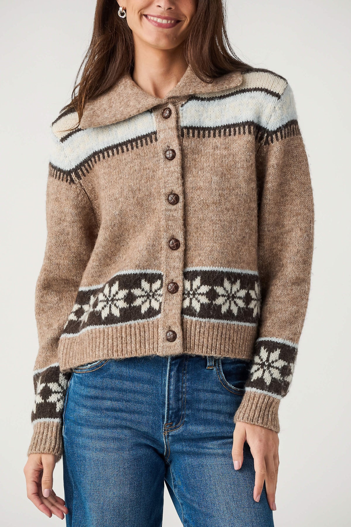 A woman wears a tan button-front cardigan with a wide collar, snowflake pattern borders, and light blue yoke, paired with jeans.