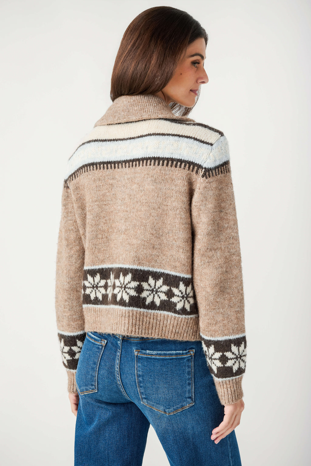 Back view of a woman wearing a tan knit collared cardigan with snowflake patterned bands and blue jeans.