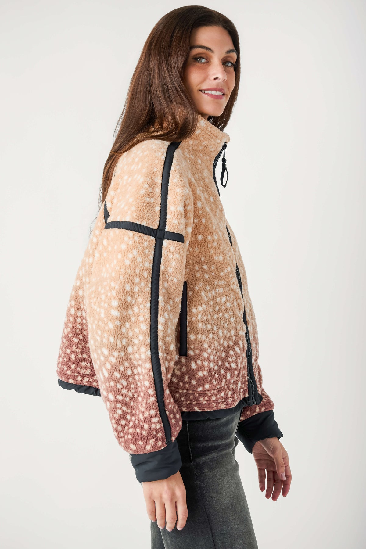 A woman wearing a tan and rose fleece jacket with cream spots and black trim looks over her shoulder.