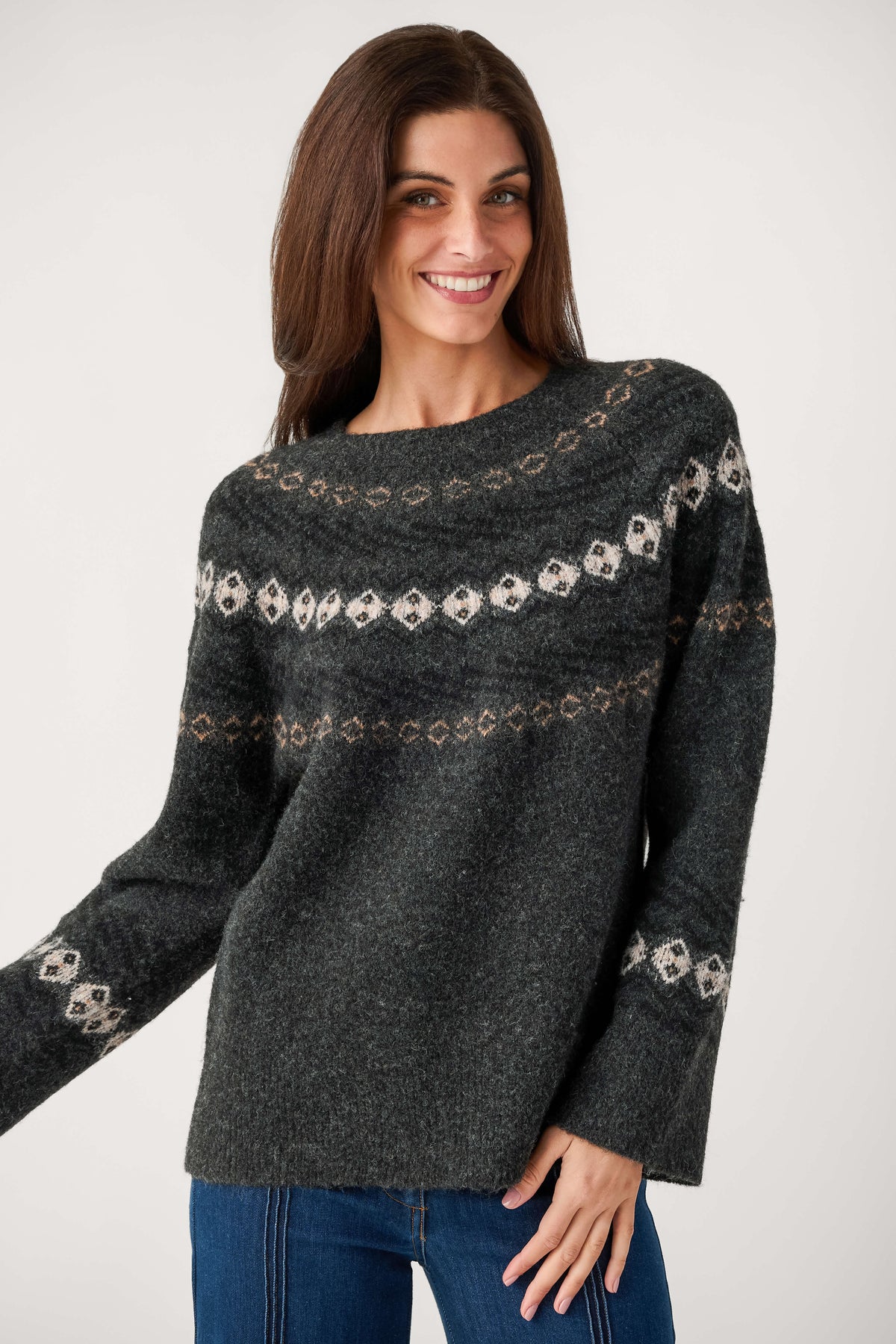 A smiling woman with long brown hair wears a charcoal gray knit sweater with cream and tan Fair Isle bands and blue jeans.