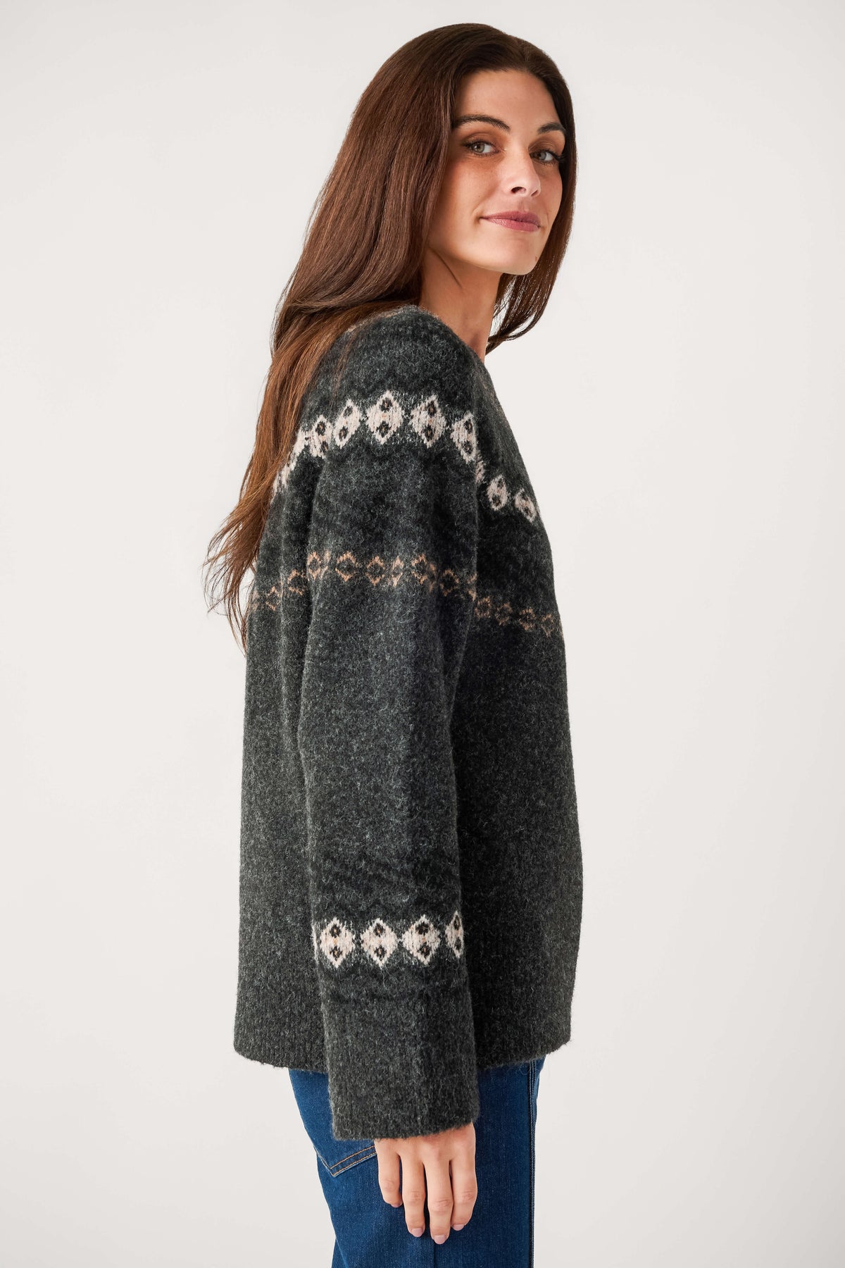 A woman with long brown hair wears a charcoal gray fuzzy sweater with cream and tan Fair Isle bands over blue jeans.