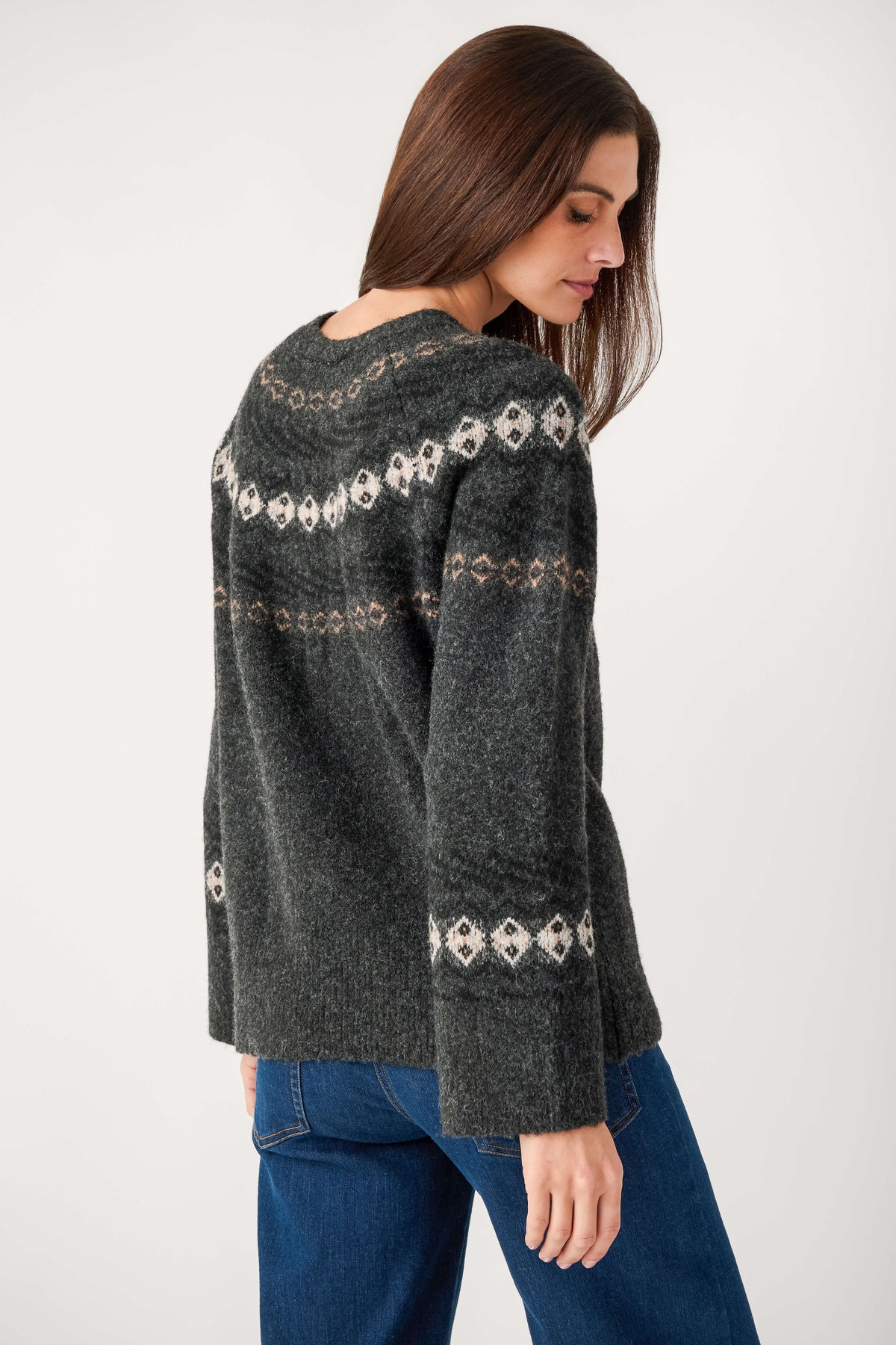 A woman with long brown hair, seen from behind, wears a charcoal Fair Isle sweater with cream patterns and blue jeans.