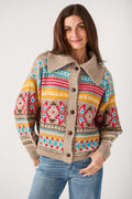 A woman wearing a beige button-front knit cardigan with colorful geometric Fair Isle patterns in red, blue, yellow, and brown, paired with blue jeans, against a light gray studio background.
