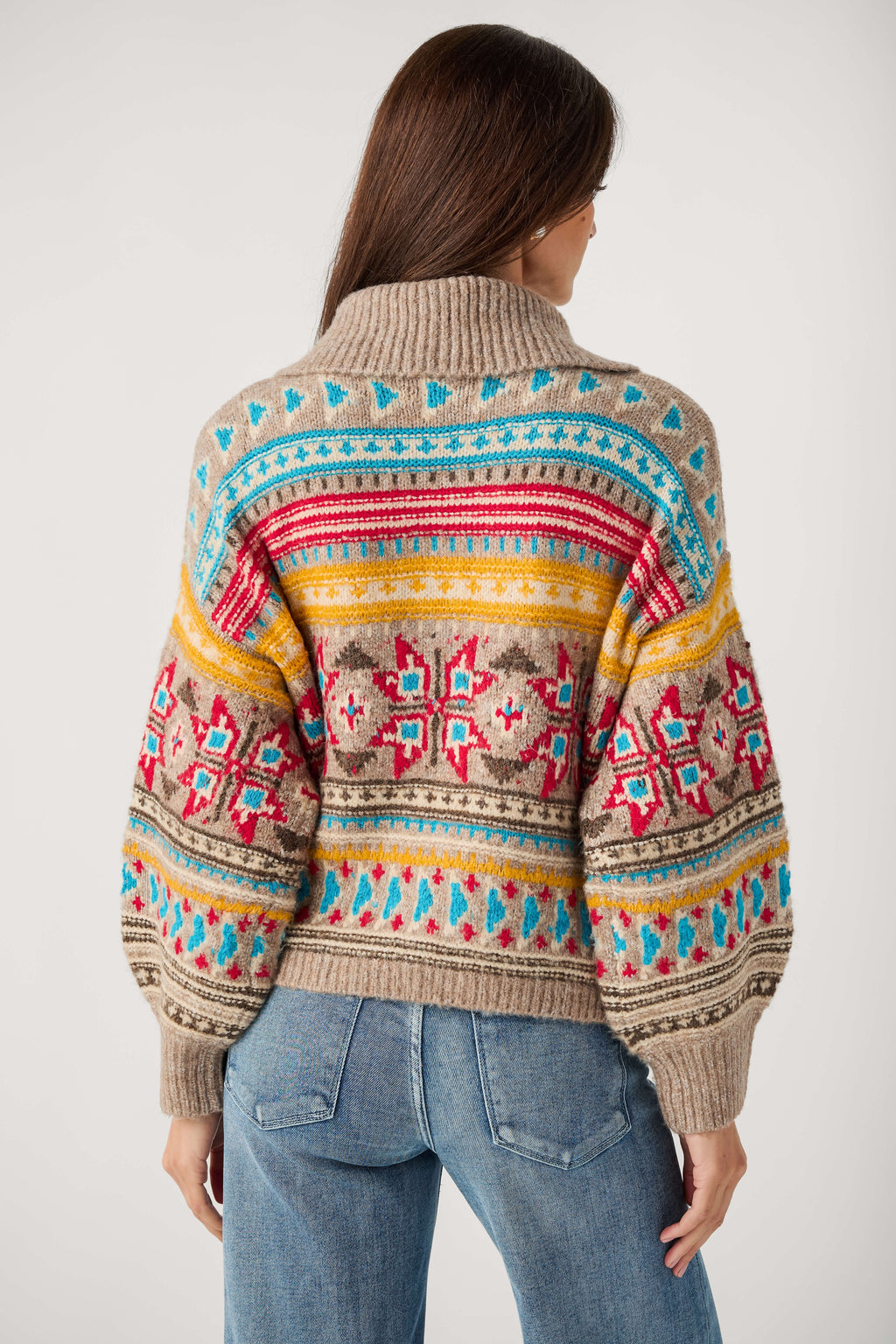 Back view of a woman wearing a taupe Fair Isle cardigan with red, turquoise and yellow patterns and blue jeans.