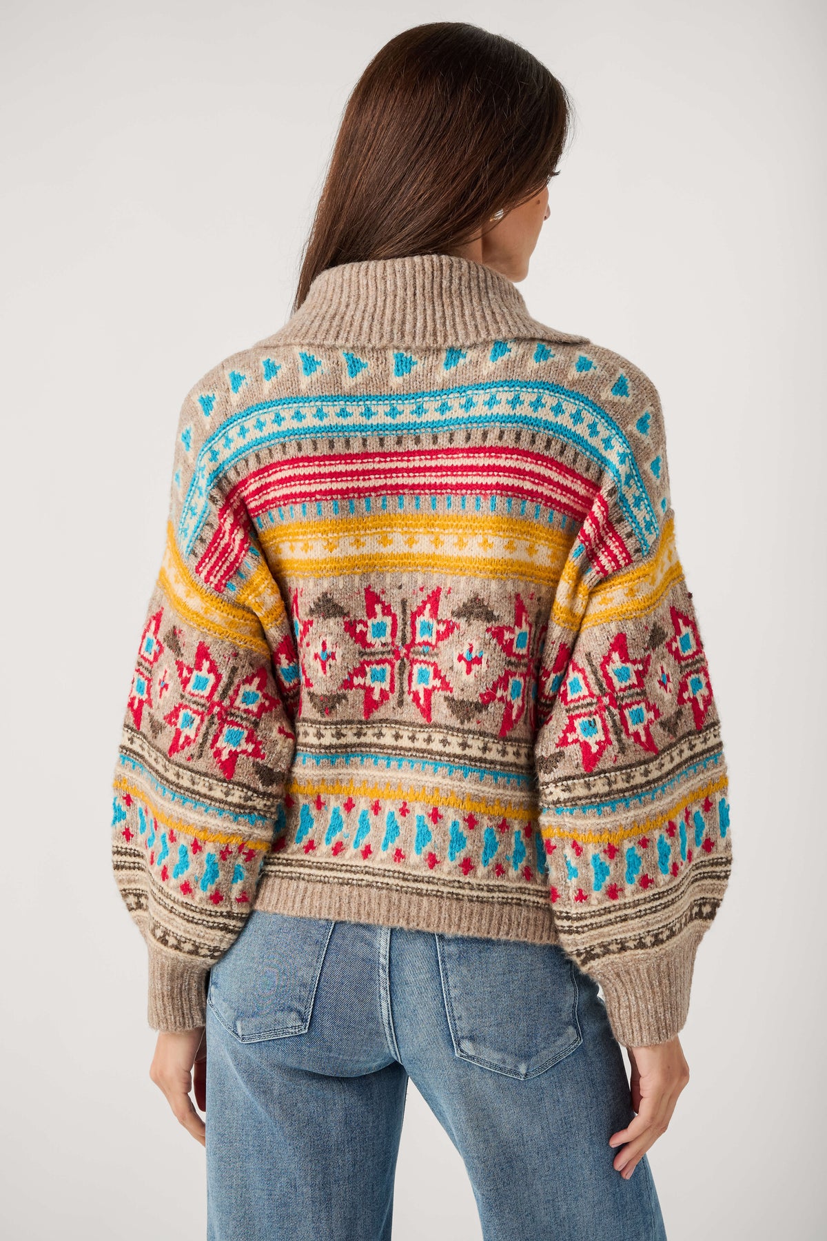 Back view of a woman wearing a taupe Fair Isle cardigan with red, turquoise and yellow patterns and blue jeans.