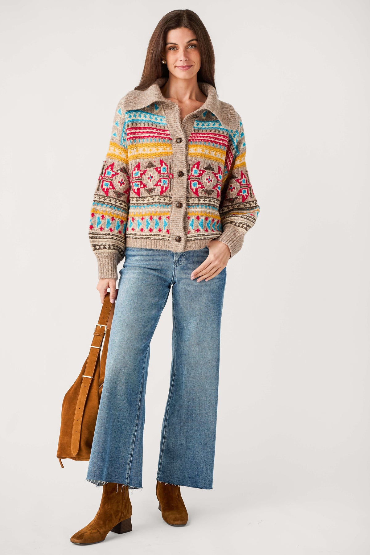 A woman wears a beige button-front cardigan with red, blue, and yellow Fair Isle patterns, wide-leg jeans, and brown suede boots.