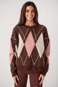 A smiling woman with long brown hair wears a fuzzy brown crewneck sweater with pink and cream argyle diamonds and matching brown pants.