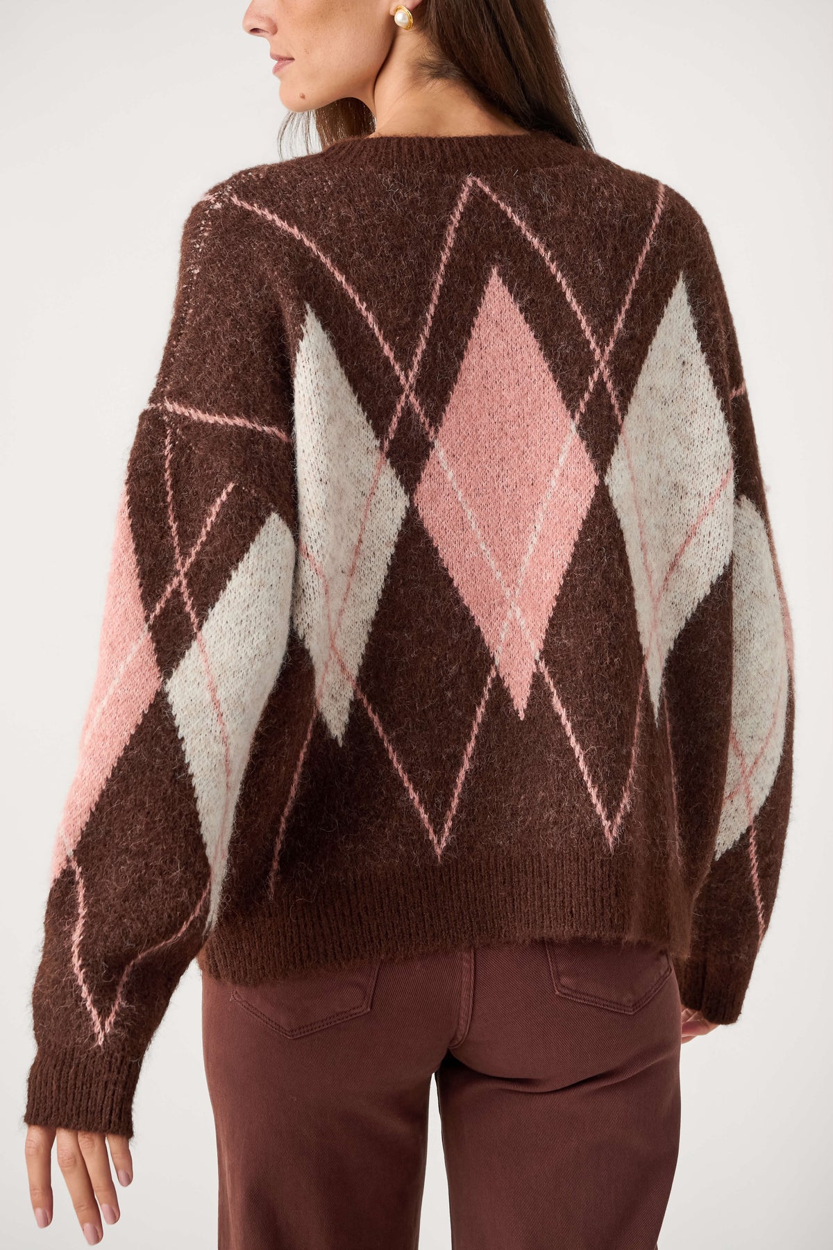 A woman seen from behind wears a fuzzy brown crewneck sweater with pink and cream argyle diamonds and brown pants.