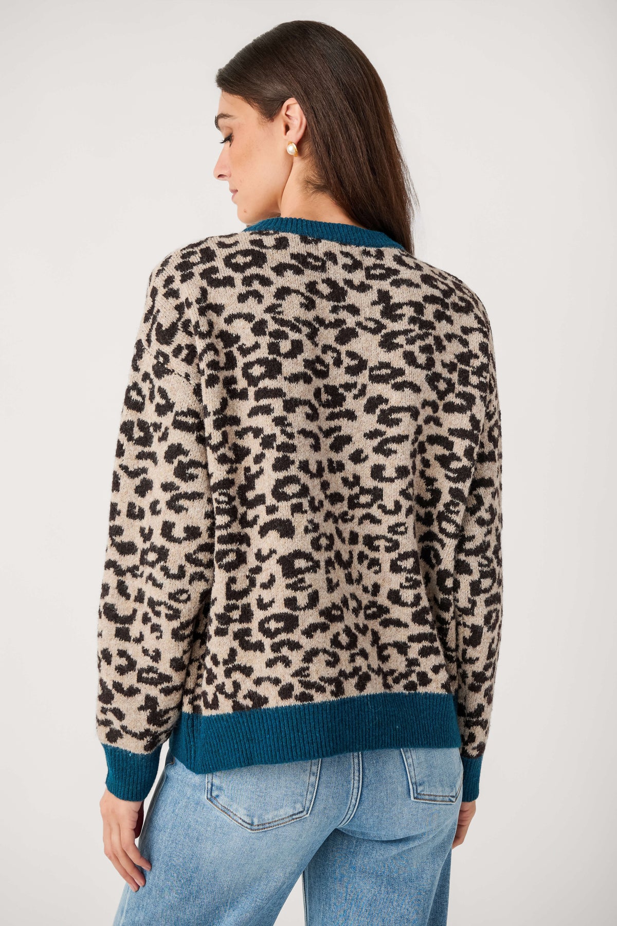 Back view of a woman wearing a beige and black leopard print knit cardigan with teal trim and light blue jeans.