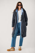 A woman wears an open dark navy hooded parka with light blue fleece lining over a white tee and jeans.