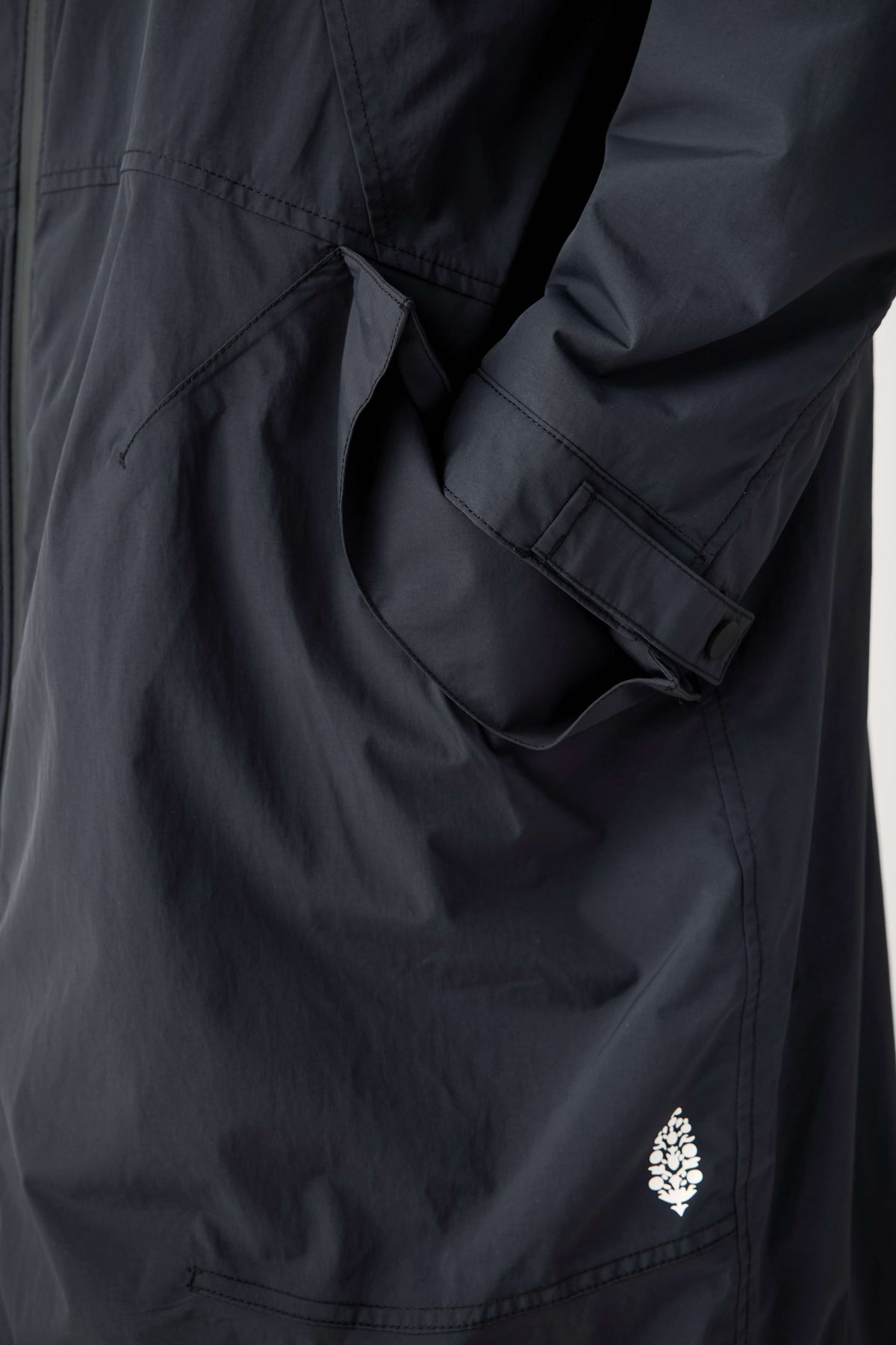 Close-up of a dark navy parka showing a front pocket, a buttoned sleeve cuff, and a small white leaf logo.