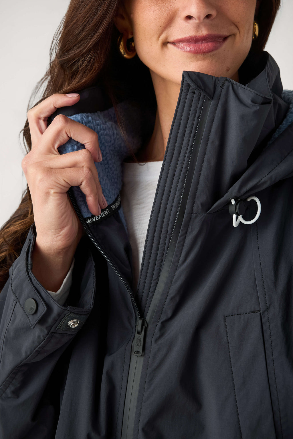Close-up of a woman wearing a dark navy parka with a blue fleece lining, partially zipped, with a white drawcord toggle.