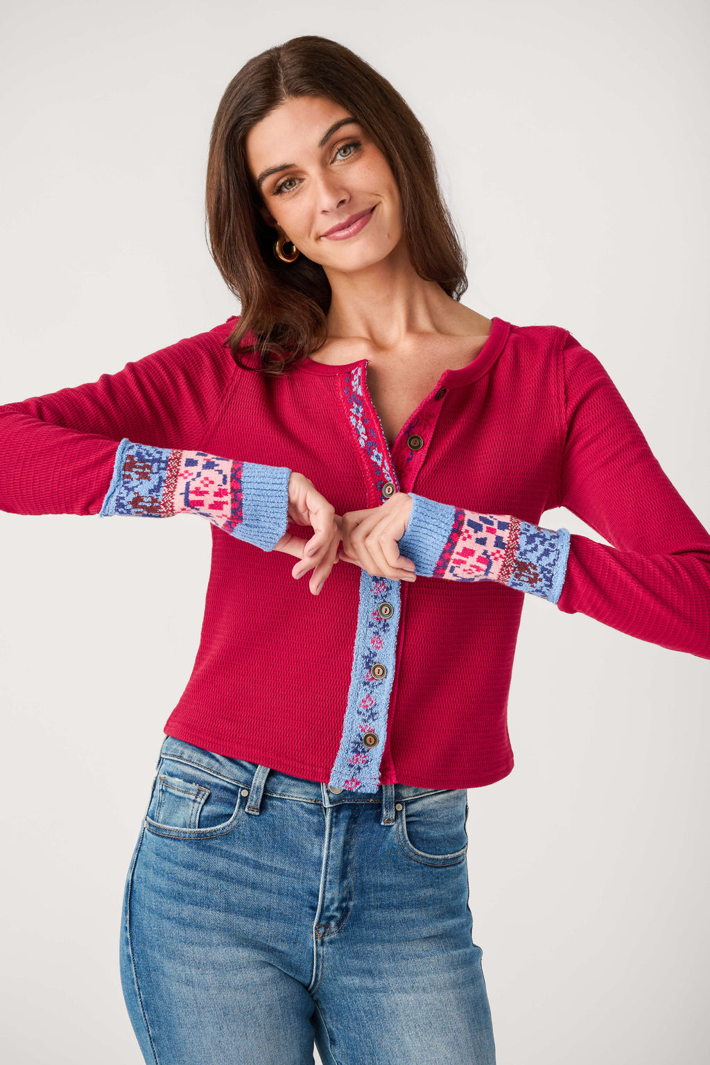 A woman wears a red waffle-knit button-front cardigan with blue patterned trim on the placket and cuffs, paired with jeans.