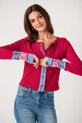 A woman wears a red waffle-knit button-front cardigan with blue patterned trim on the placket and cuffs, paired with jeans.