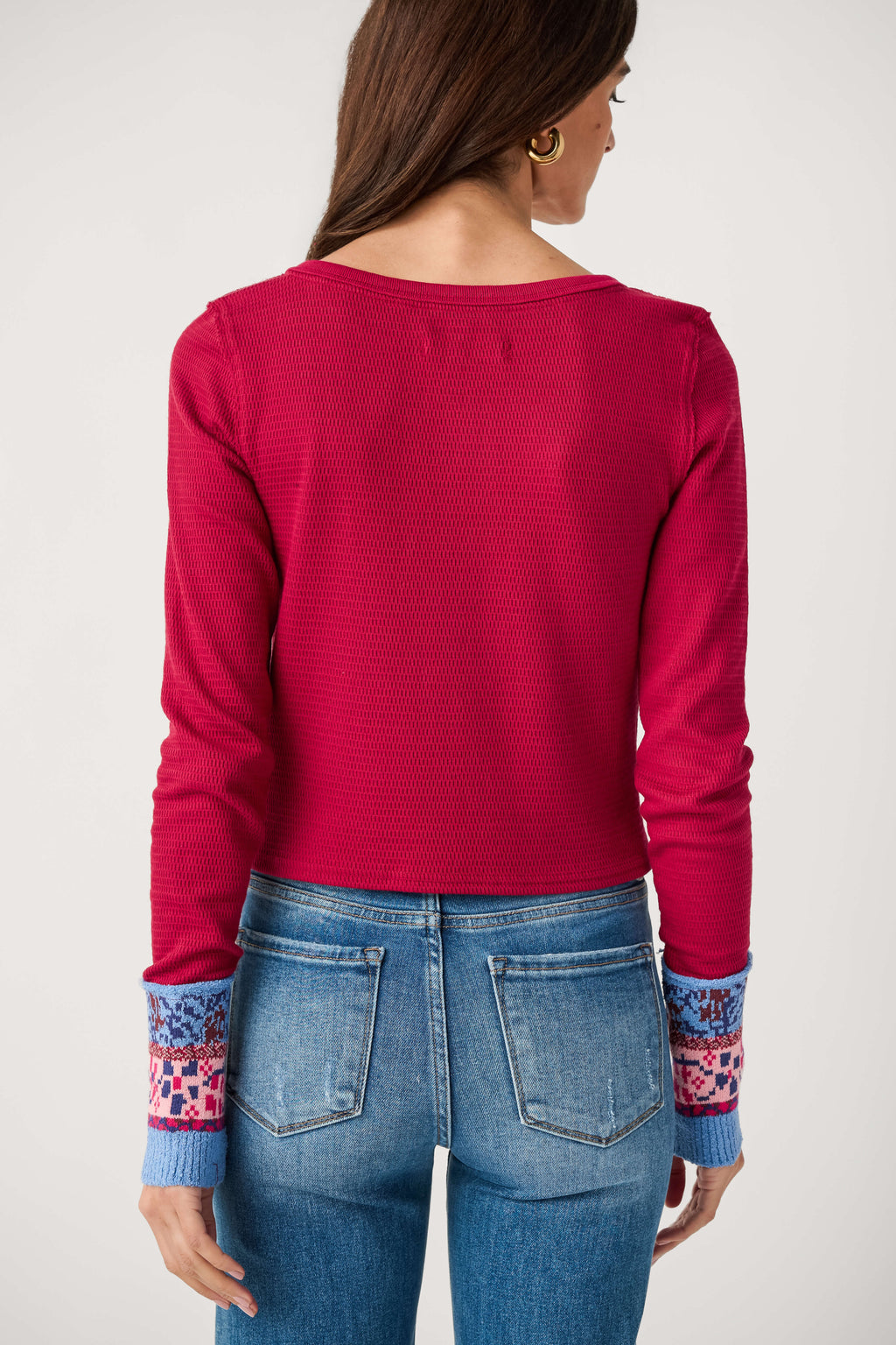 A woman seen from behind wears a cropped red waffle-knit top with patterned blue and pink cuffs and light-wash jeans.