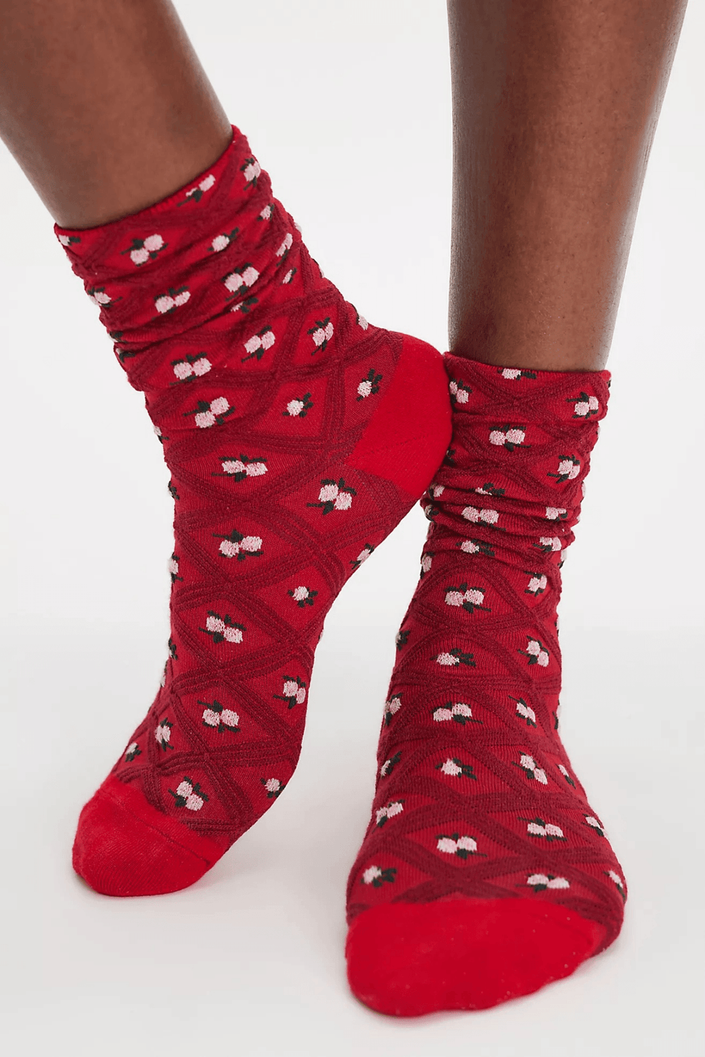 Red crew socks with a diamond lattice texture and small pink floral motifs are worn on a pair of feet.