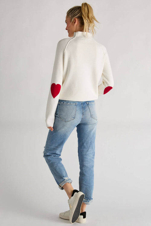 White knit sweater with high neck and red heart patches on sleeves, cuffs ribbed